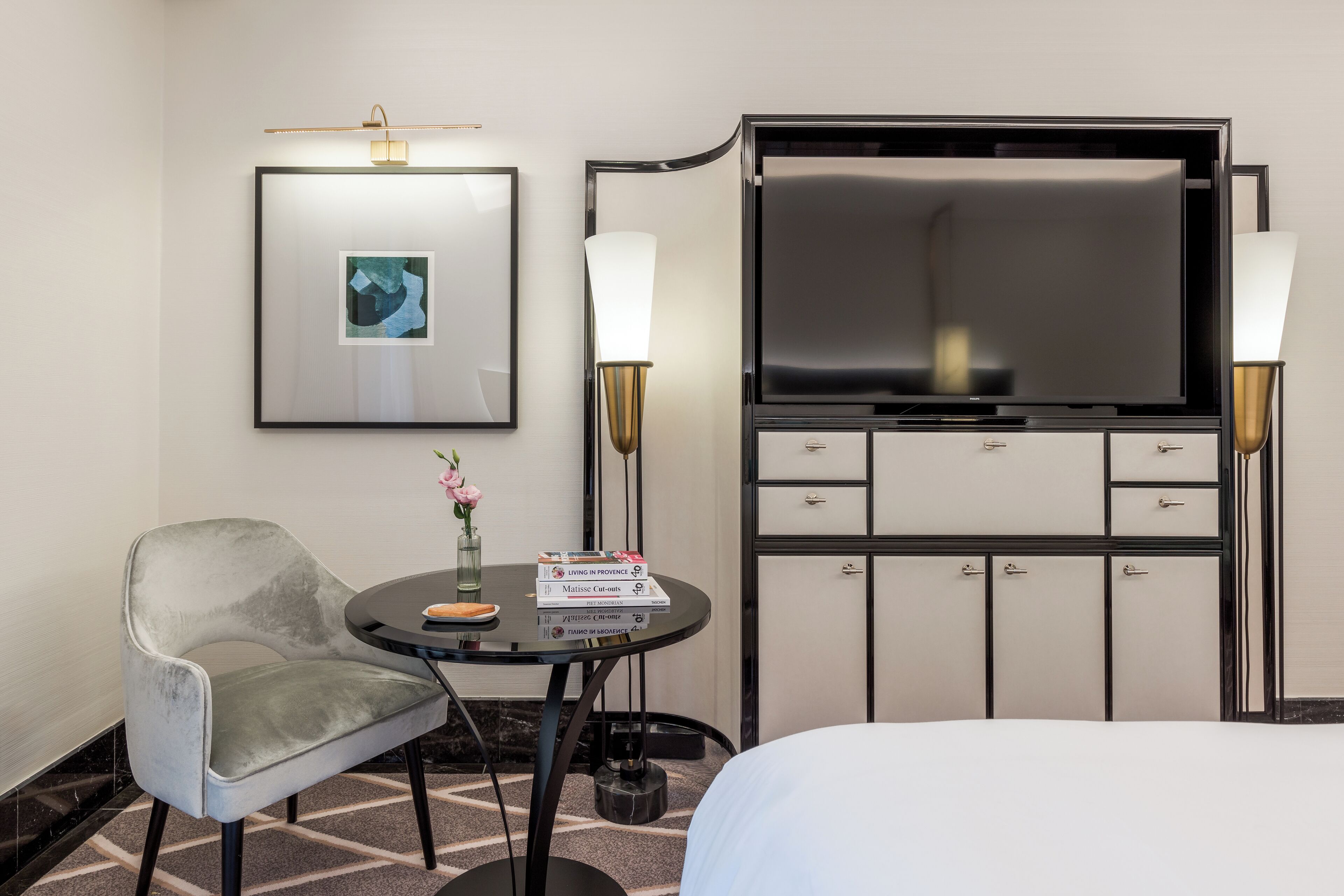 Habitación de hotel con cama, escritorio con silla, televisión, un cuadro enmarcado y una lámpara.
