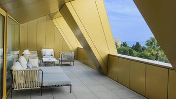 Ein Balkon mit einer Sitzecke, inklusive Sofa, Stühlen und Tisch, mit Blick auf die Küste.