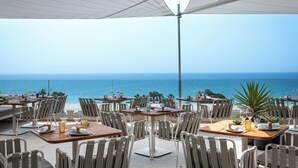 An outdoor dining area with tables and chairs, overlooking the sea.