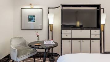 Habitación de hotel con cama, escritorio con silla, televisor, minibar y un cuadro en la pared.
