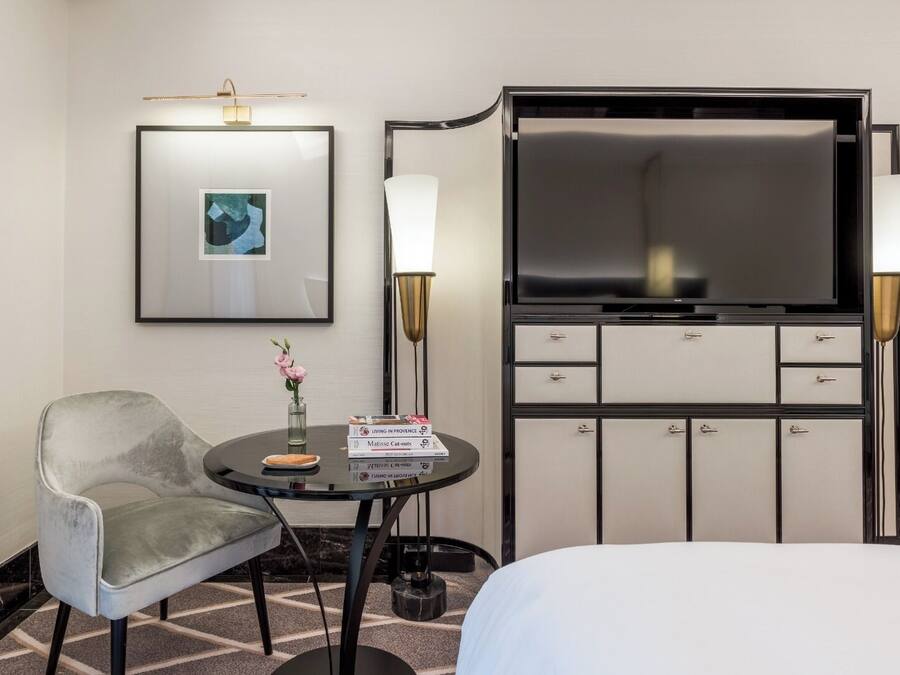 Habitación de hotel con cama, escritorio con silla, televisor, minibar y un cuadro en la pared.