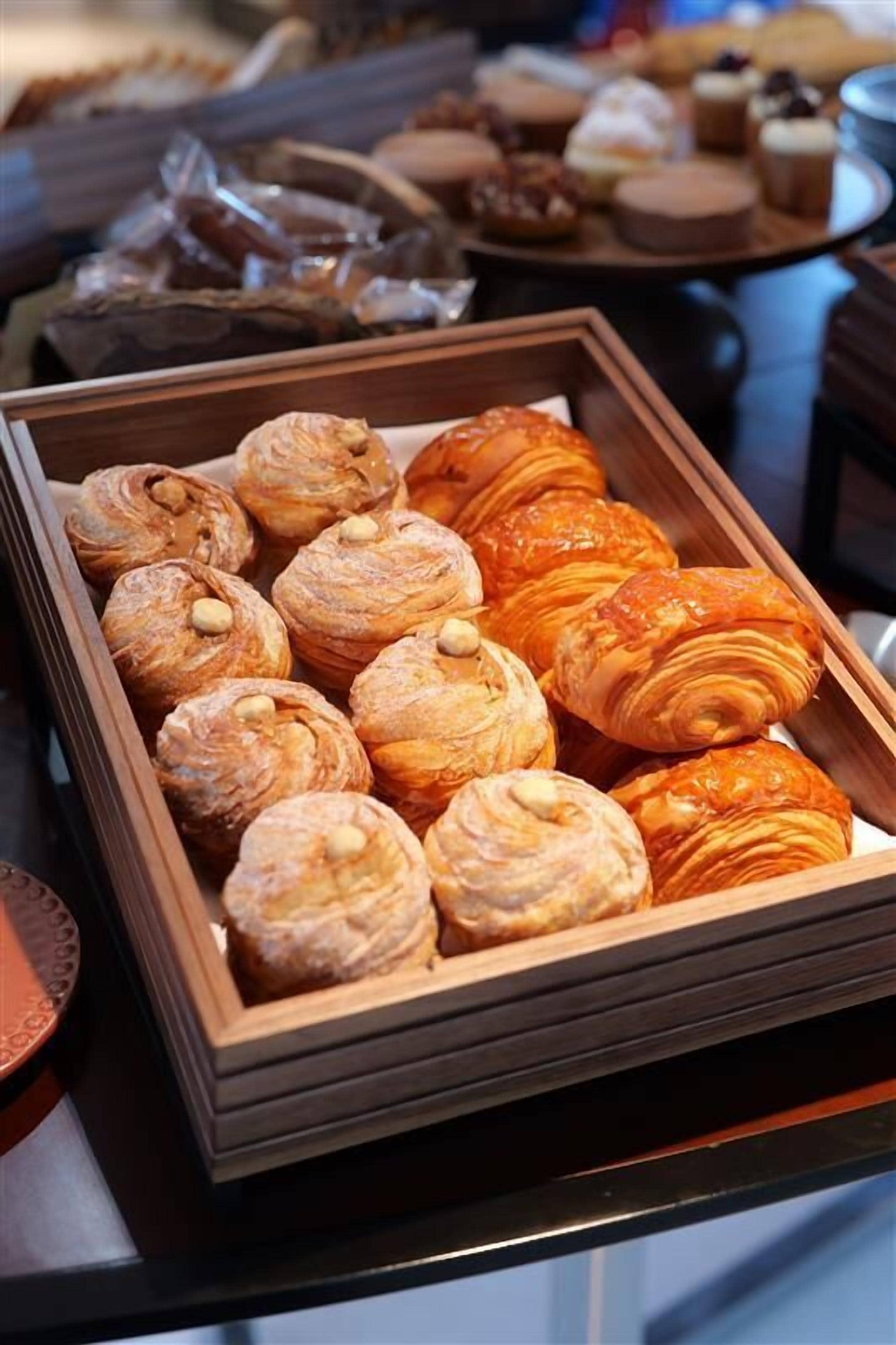 Una bandeja con varios pasteles, incluyendo croissants y hojaldres, sobre un soporte de madera.