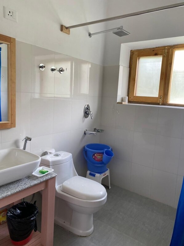 A bathroom with a white sink, toilet, and blue bucket. - Osay Khar Resort (Leh)
