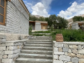 A stone staircase leading to a building with a wooden door and a stone wall on the right. - Osay Khar Resort (Leh)