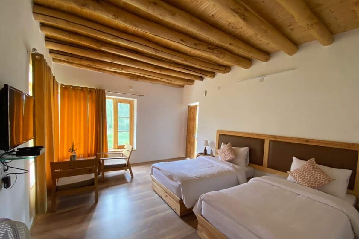 A room with two beds, wooden ceiling beams, a desk, and a window with curtains.