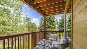 A covered balcony with a table and chairs, surrounded by trees.
