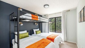 A modern hotel room with a bunk bed, two single beds, a large window with a view, and a ceiling light.