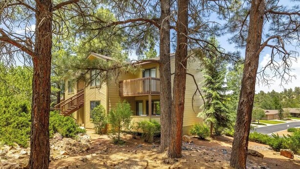 A two-story house with a balcony, surrounded by pine trees and a rocky landscape.