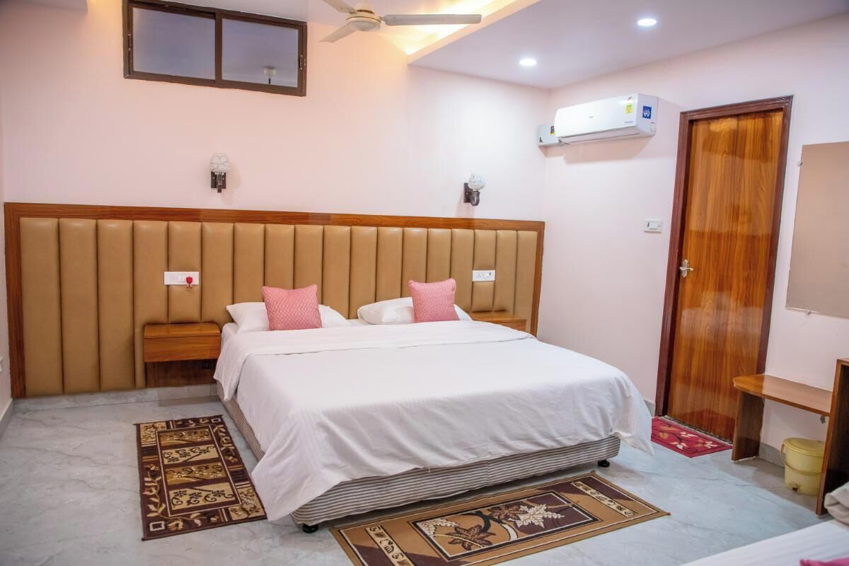Un dormitorio con una cama grande, un cabecero de madera, una mesita de noche y una lámpara de noche, un aire acondicionado de pared, un ventilador de techo y una puerta.