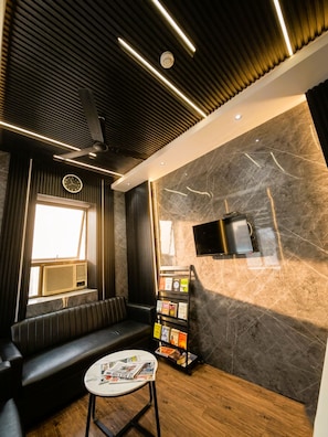 Un intérieur moderne avec un canapé, une petite table sur laquelle sont posés des magazines, une bibliothèque et un téléviseur fixé au mur.