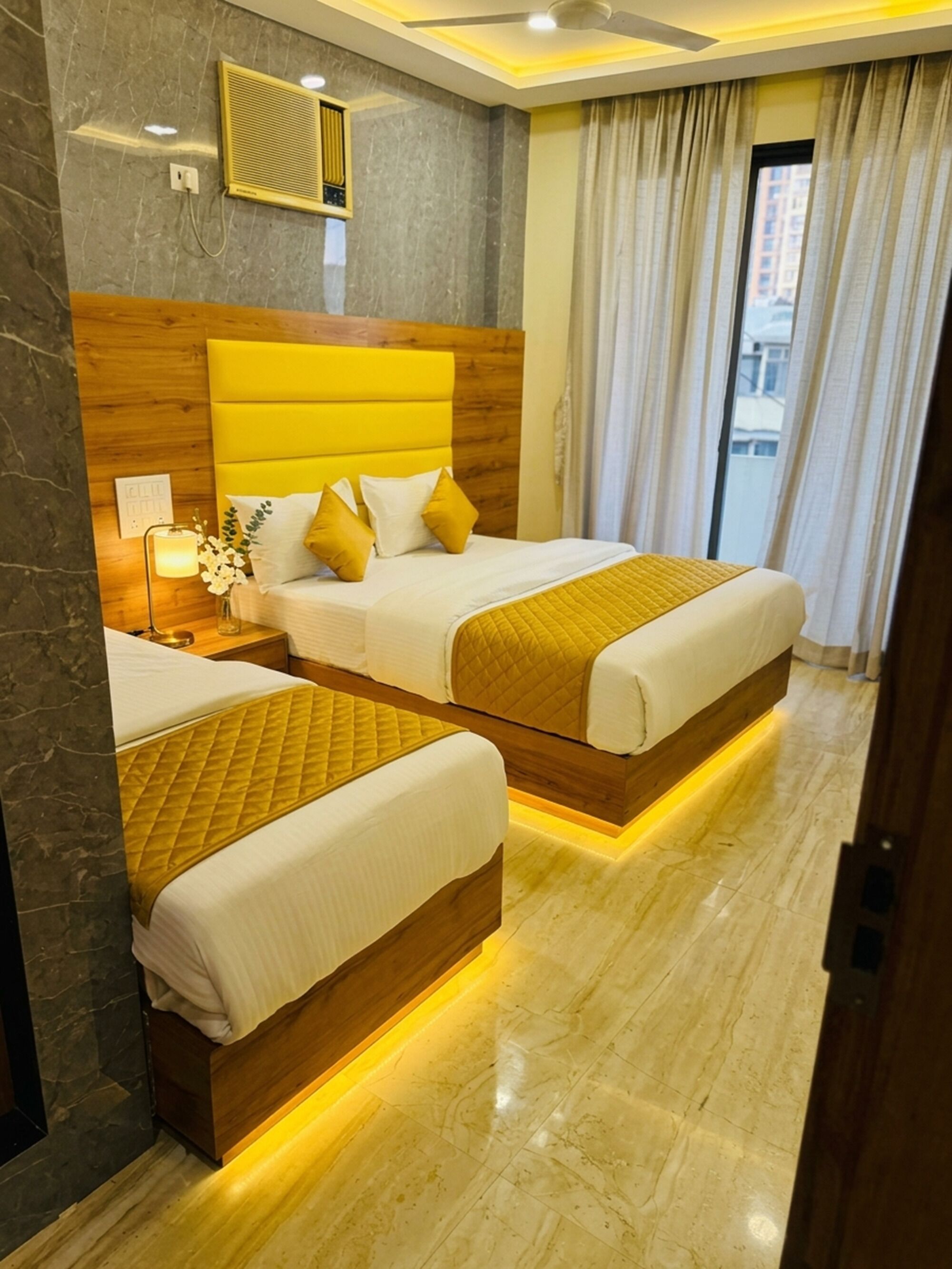 A hotel room with two beds, marble flooring, a wooden headboard, a ceiling fan, and a window with curtains.