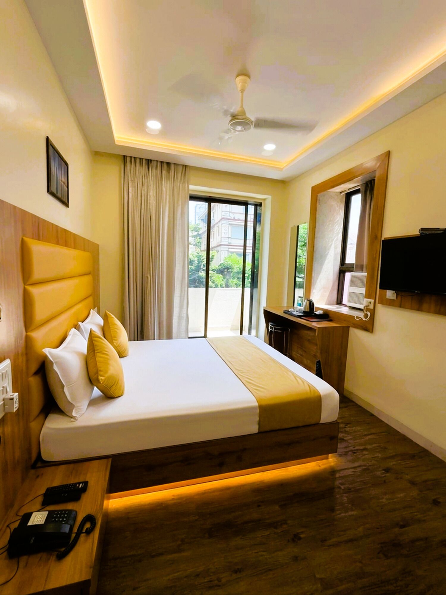 Une chambre d’hôtel équipée d’un lit, d’un bureau, d’un téléphone, d’une télévision et d’un ventilateur de plafond.