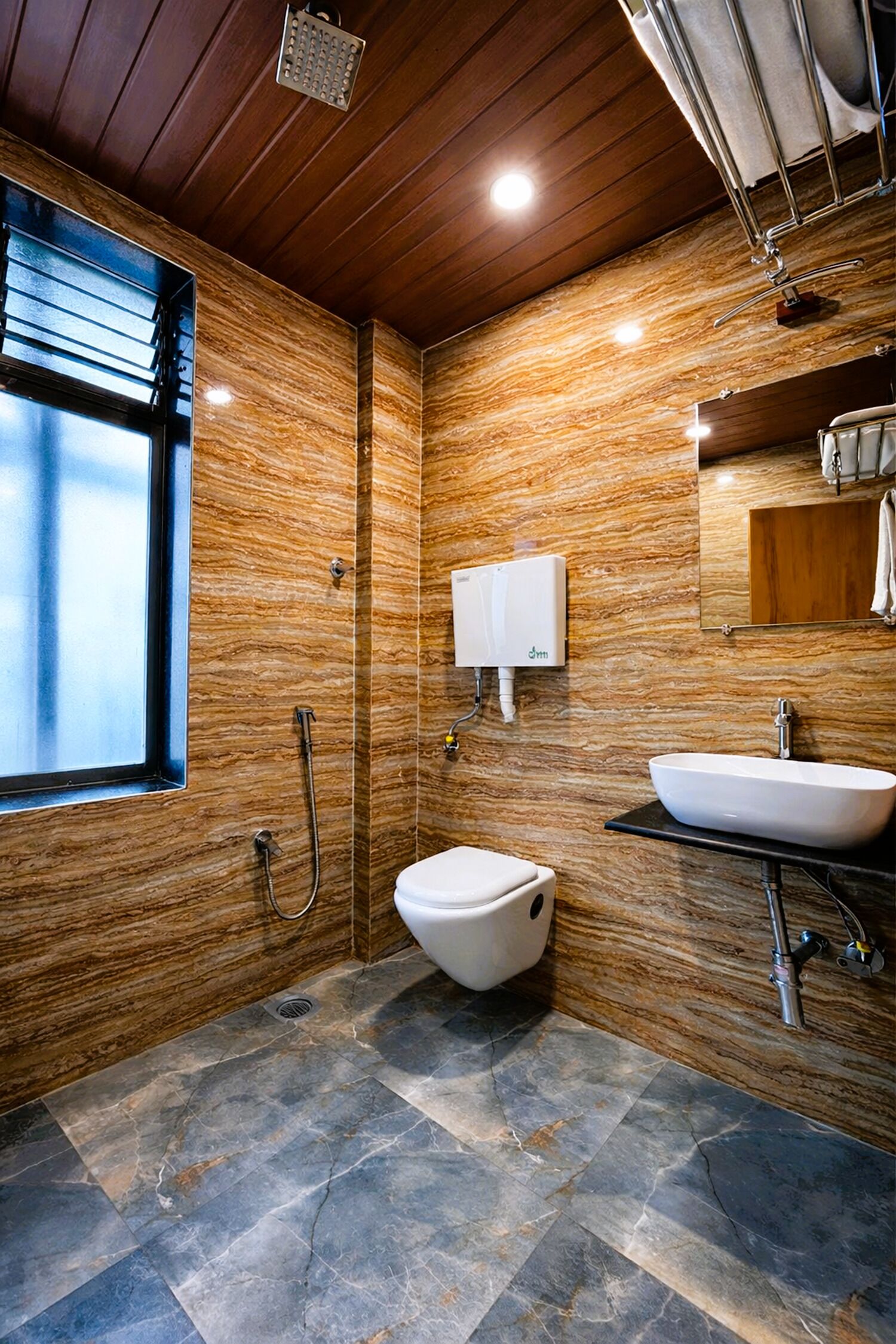 A bathroom with a marble wall, a white sink, a toilet, and a shower.