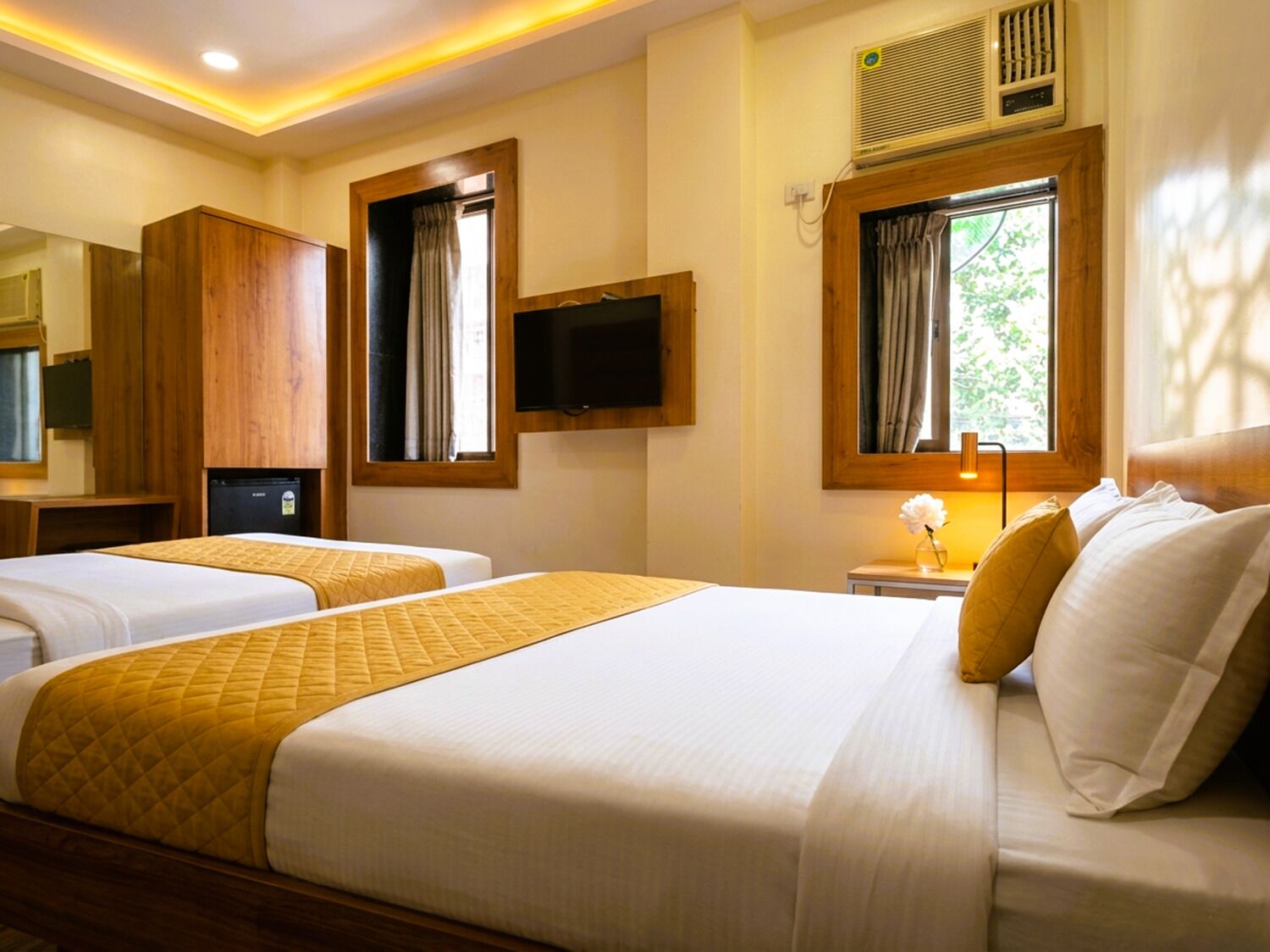 A hotel room with two beds, a television, an air conditioning unit, and a window with curtains.