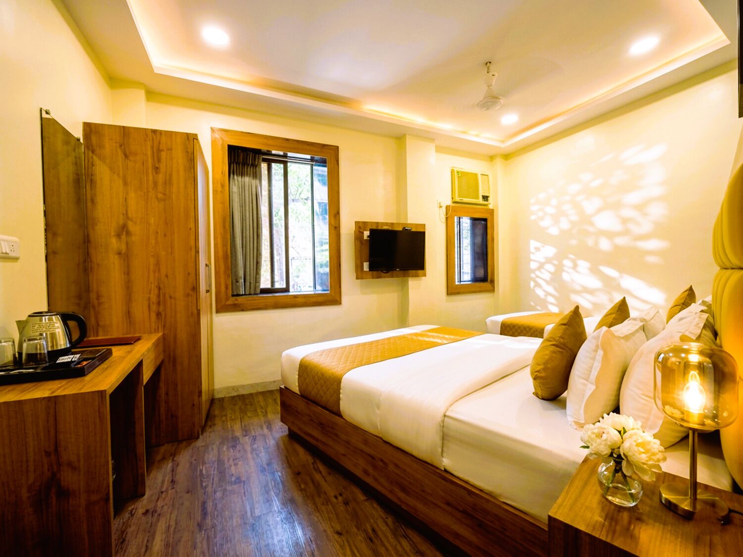 A hotel room with a bed, bedside table, TV, window, and wooden flooring.