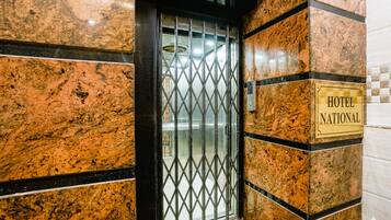 Entrada de un hotel con una puerta de metal, un letrero que dice 'HOTEL NATIONAL' y paredes de mármol.