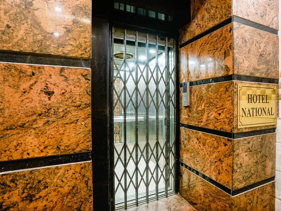 Entrada de un hotel con una puerta de metal, un letrero que dice 'HOTEL NATIONAL' y paredes de mármol.