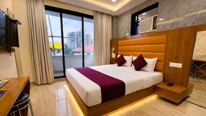 Une chambre d’hôtel avec un grand lit, un bureau, une télévision et une vue sur les immeubles par la fenêtre.