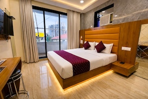 A hotel room with a large bed, a desk, a TV, and a view of buildings through the window. - Hotel National  (Mumbai)