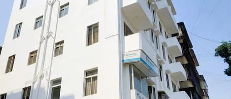 A multi-story building with a white facade, a visible balcony on the second floor, and a sign for 'Reliance Digital' on the ground floor.