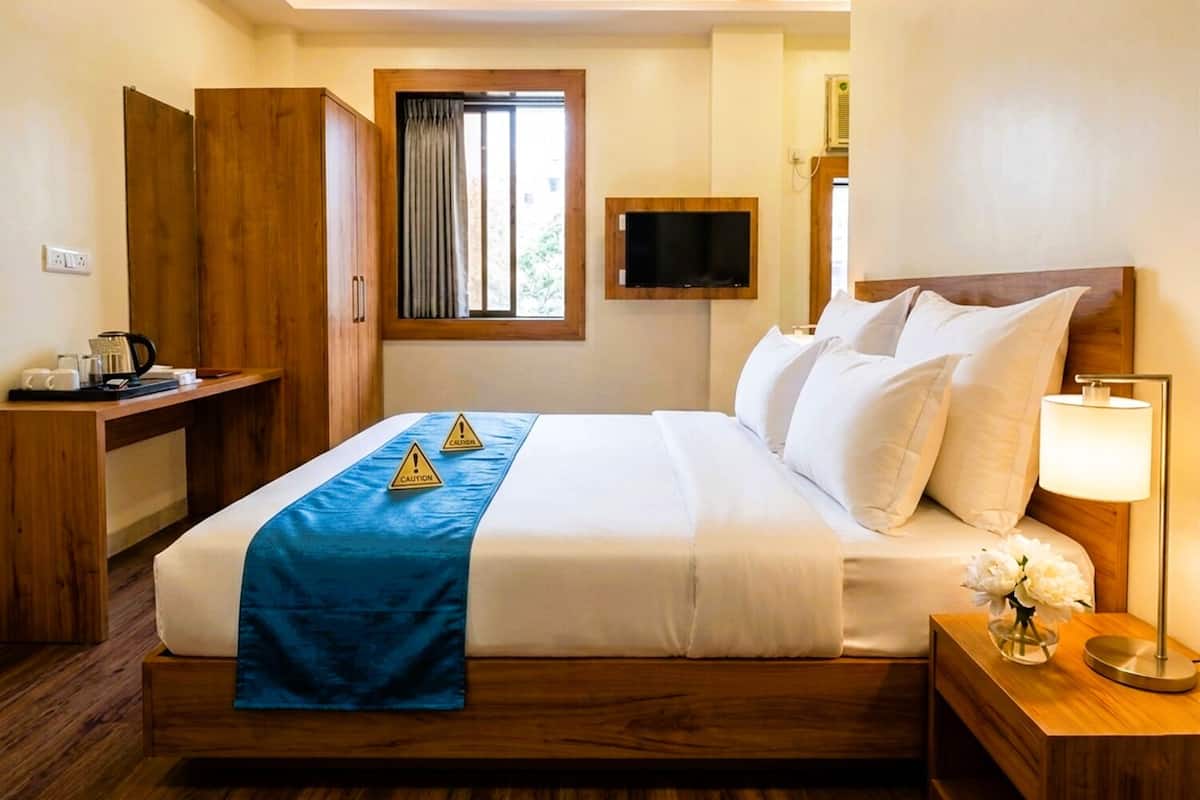 Ein Hotelzimmer mit Bett, Nachttisch, Fernseher und einem Fenster mit Vorhängen.
