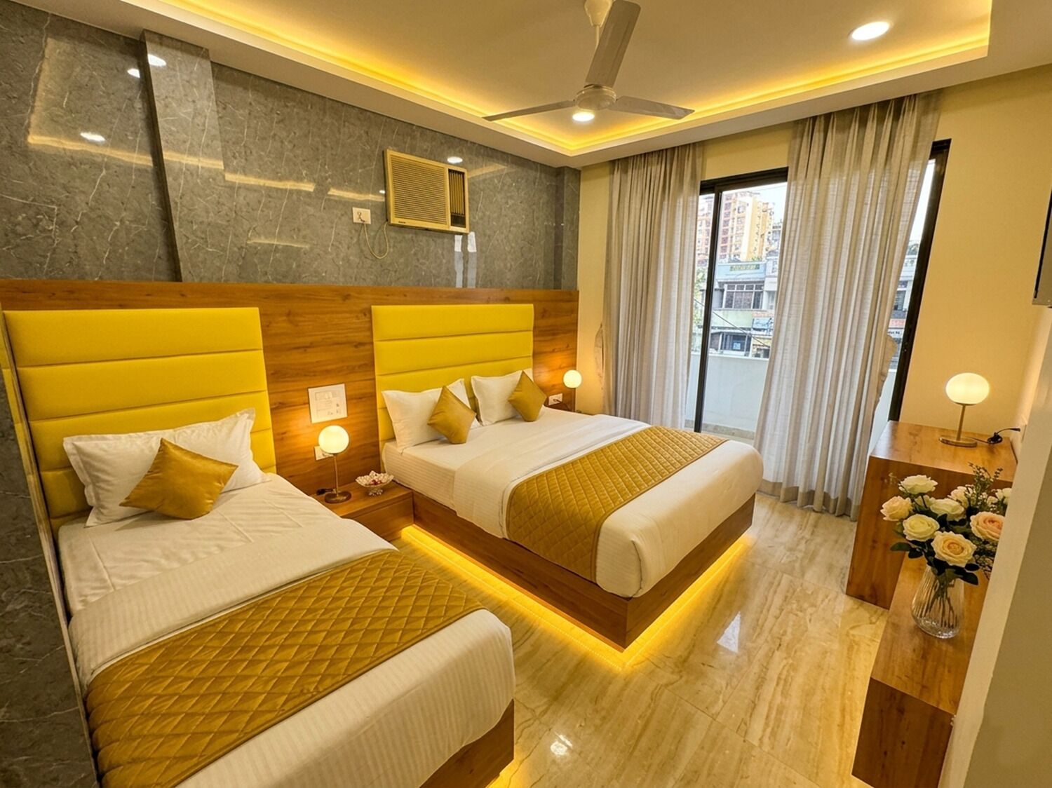 A hotel room with two beds, a ceiling fan, a window with curtains, and a nightstand with a lamp.
