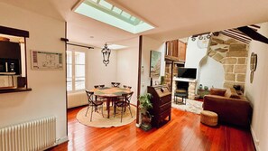 Relax in this spacious living area with a dining table, sofa, and armchairs, featuring a fireplace and large window with an outdoor view.