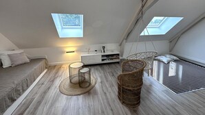 A modern loft bedroom with skylights, a bed, a seating area, and a small table.