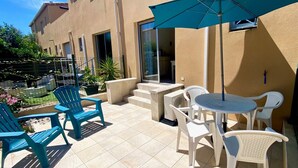 An outdoor patio with a table and chairs, a blue umbrella, and a small garden area.