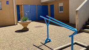 A courtyard with a blue railing, a potted plant, and a building with blue doors.