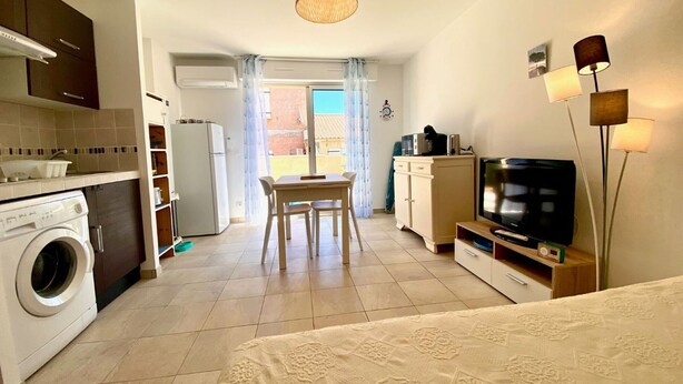 A compact hotel room with a kitchenette, a dining area, a TV, and a bed.