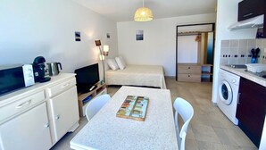A compact hotel room with a kitchenette, a dining area, a bed, and a washing machine.