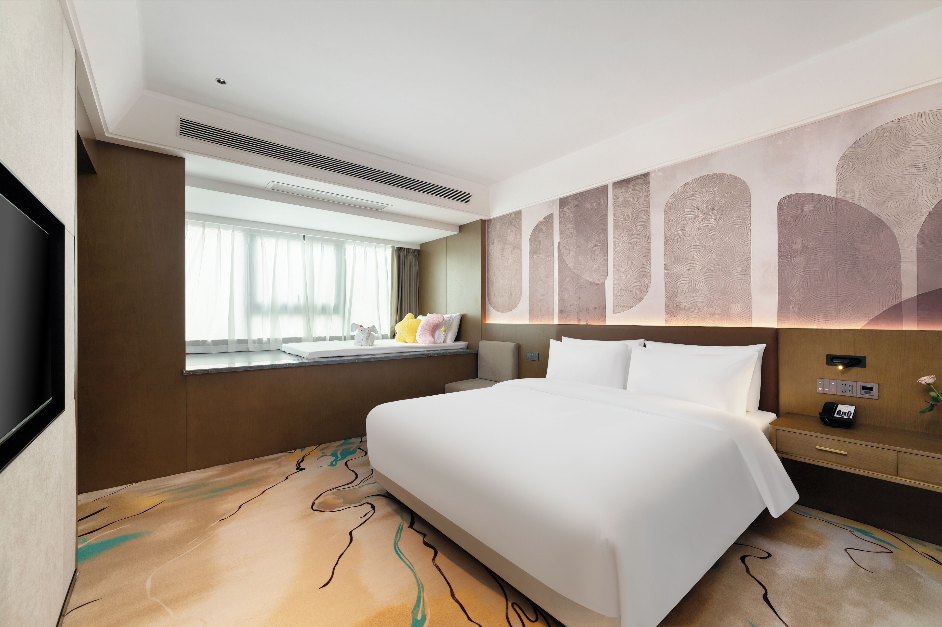 Habitación de hotel con una cama grande, un televisor de pantalla plana montado en la pared, una ventana con cortinas y una pared decorada con motivos abstractos.