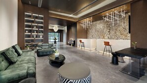 A modern lobby with a sectional sofa, a round ottoman, a dining area with a black table, and a decorative wall with a geometric light fixture. - RunhaoHOTEL (Chengdu)