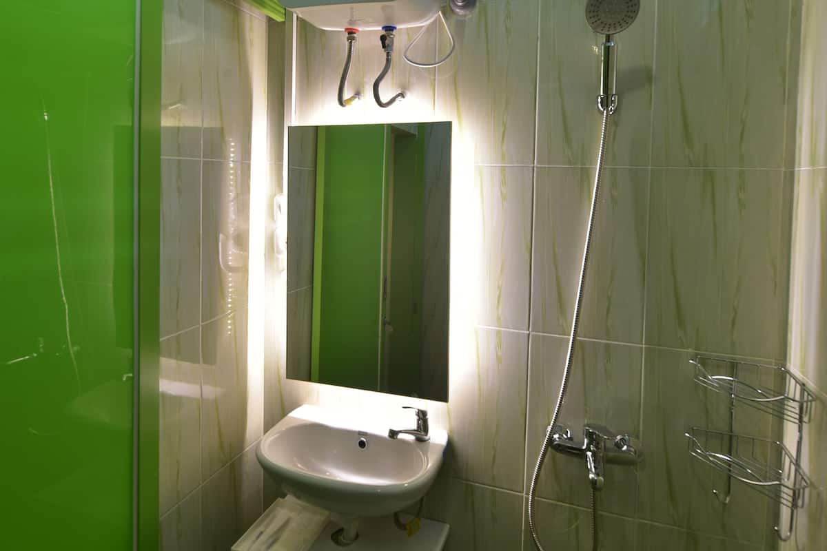 Ein Badezimmer mit grünen Fliesen, einem weißen Waschbecken, einem Spiegel und einer Dusche mit Duschbrause.