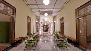 A hallway with green chairs and tables, a tiled floor, and a decorative archway at the end. - Hotel Irian Surabaya (Surabaya)