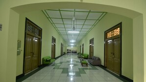 A hallway with green and white tiled floors, wooden doors, and green and gray seating areas. - Hotel Irian Surabaya (Surabaya)