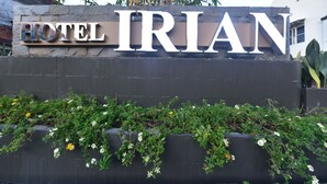 A sign for Hotel Irian with a stone facade and a garden with white and yellow flowers in front. - Hotel Irian Surabaya (Surabaya)