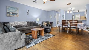 Ein Wohnzimmer mit grauem Sofa, einem Couchtisch und einem Essbereich mit Tisch und Stühlen.