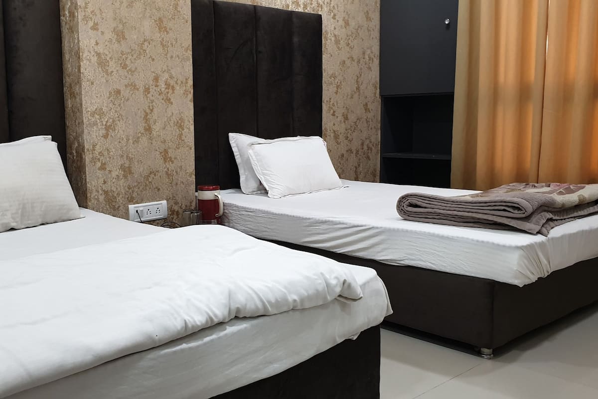 Two beds with white linens, a power outlet, and a folded blanket on the right bed.