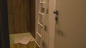 A narrow hallway with a wooden floor, a white door, and a white ladder leaning against the wall.