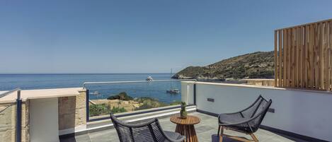 A balcony with two wicker chairs, a small round table, and a view of the sea and a boat in the distance.