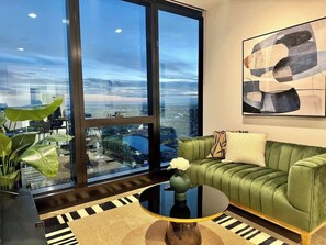 A modern living room with a green sofa, a round coffee table, and a large window offering a city view.