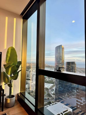 Quarto com uma janela grande, uma planta em vaso e vista para a cidade.