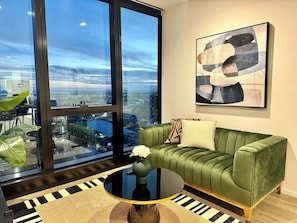 Uma sala de estar moderna com um sofá verde, uma mesa de centro redonda e uma janela grande com vista para a cidade.