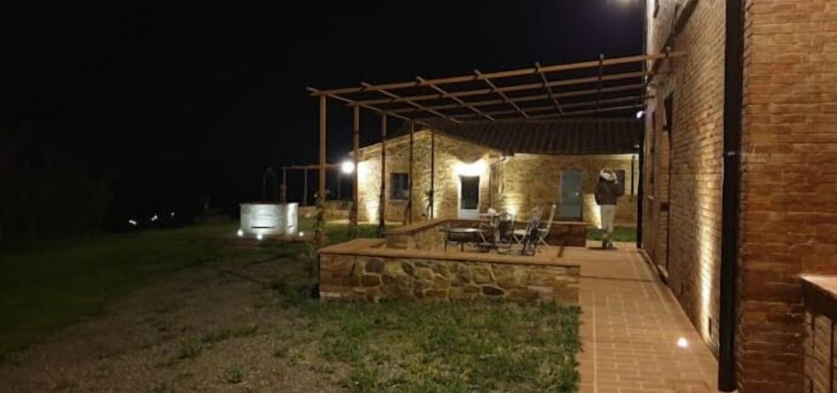 Un espacio al aire libre con patio, una banca de piedra y una mesa, rodeado por una pérgola de madera.