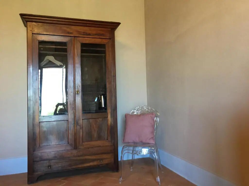 Un armario de madera con puertas de vidrio y una silla transparente con un cojín rosa.