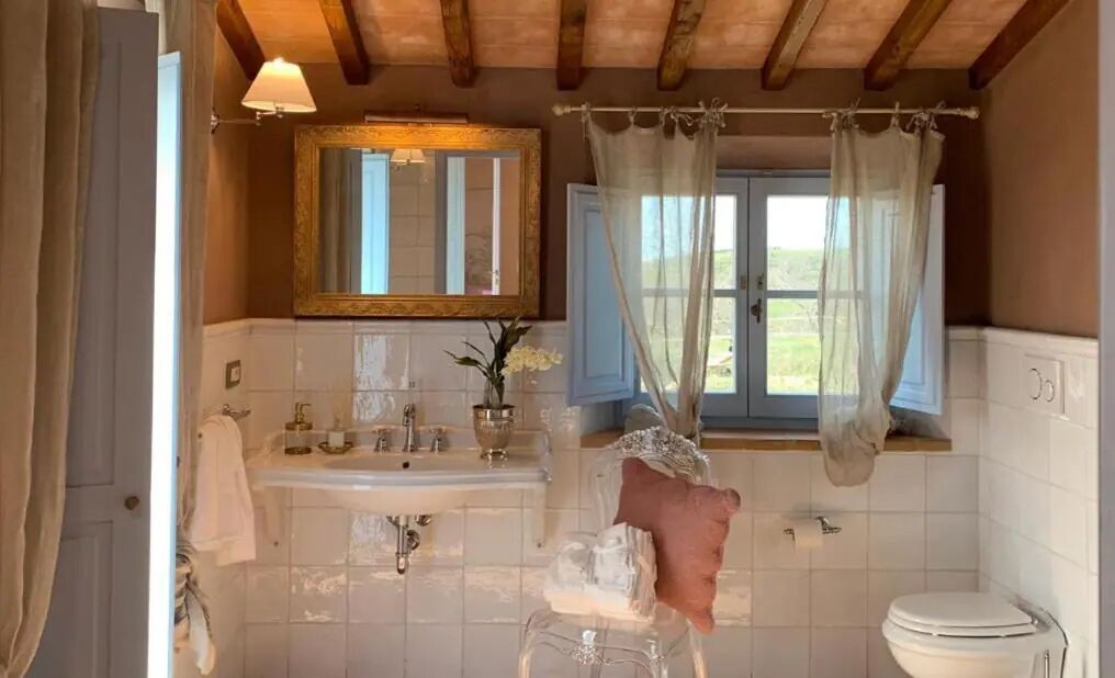 Un baño con techo de madera, un espejo grande, un lavabo, un inodoro y una ventana con cortinas.