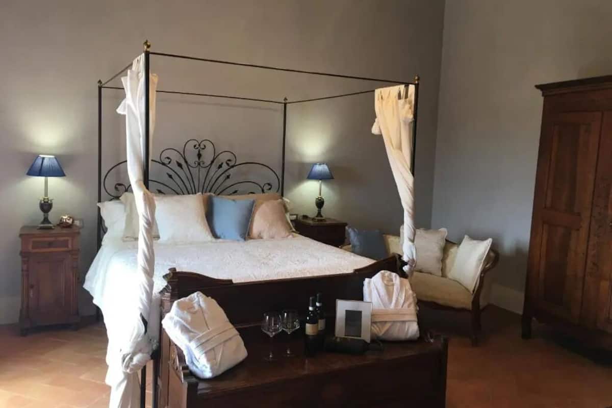 A four-poster bed with a canopy, bedside tables with lamps, a wooden nightstand, and a wooden wardrobe.