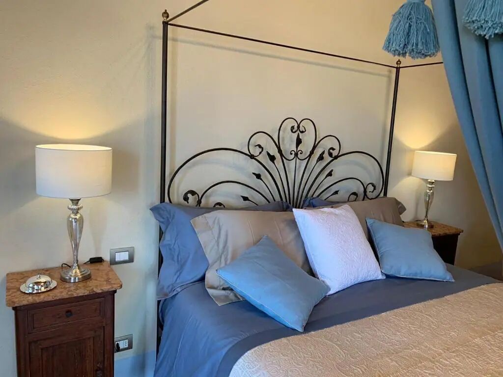 A neatly made bed with a metal headboard, two bedside tables with lamps, and a blue curtain.